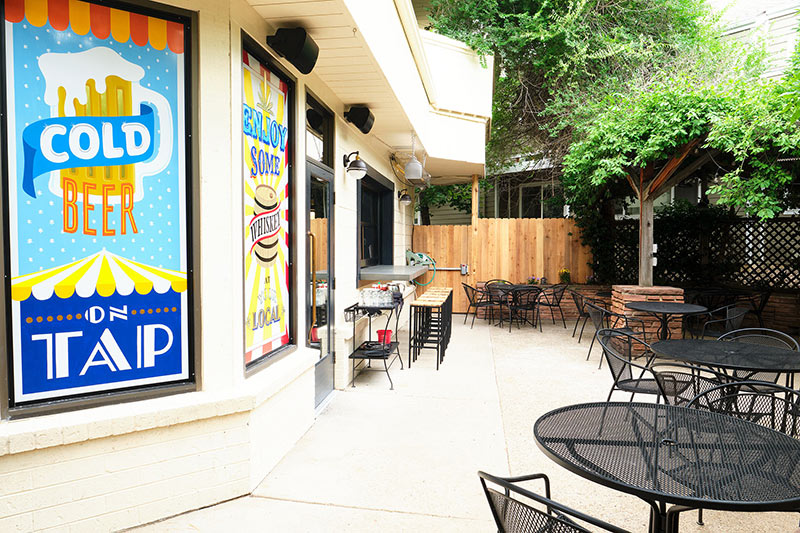 A patio with bar stools, tables & chairs and colorful posters on the wall.